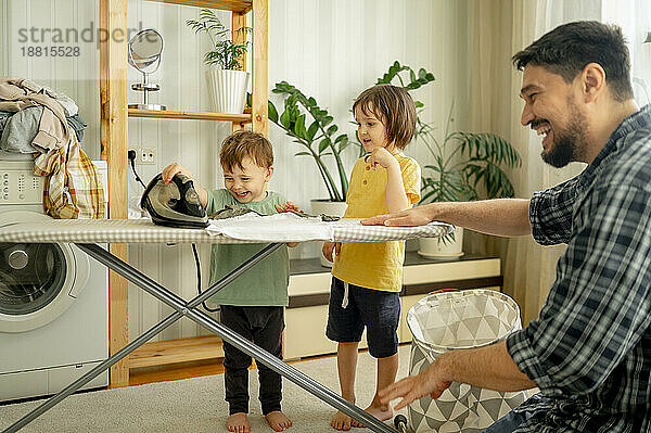 Happy children helping father ironing clothes at home