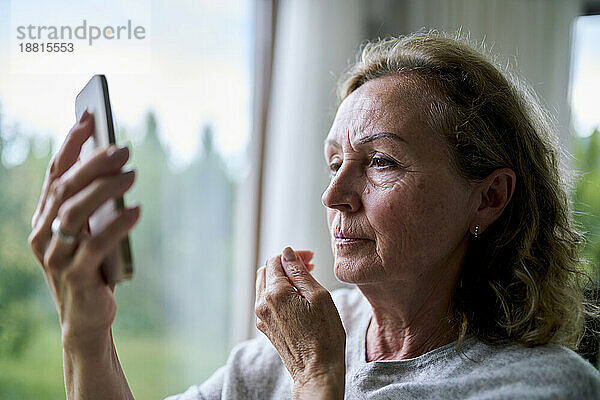 Ältere Frau schaut zu Hause auf ihr Smartphone