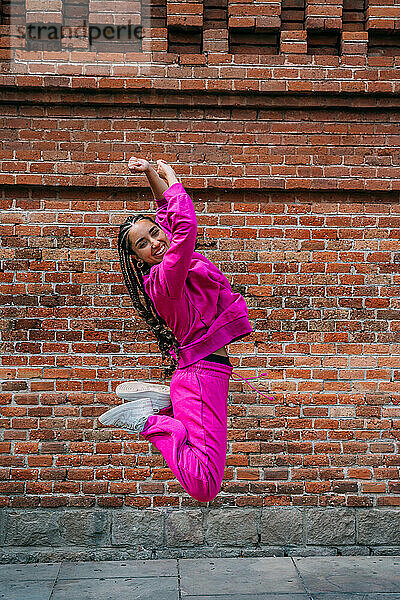 Lächelnde Frau springt vor Ziegelmauer