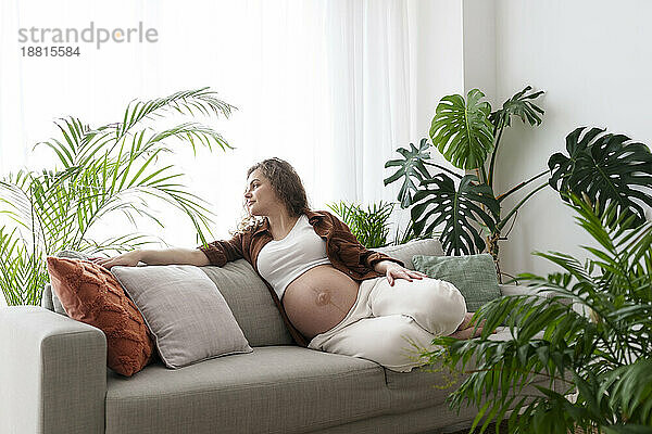 Young pregnant woman spending leisure time sitting on sofa at home