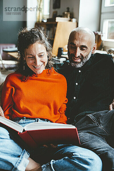 Happy woman sharing book with man sitting at home