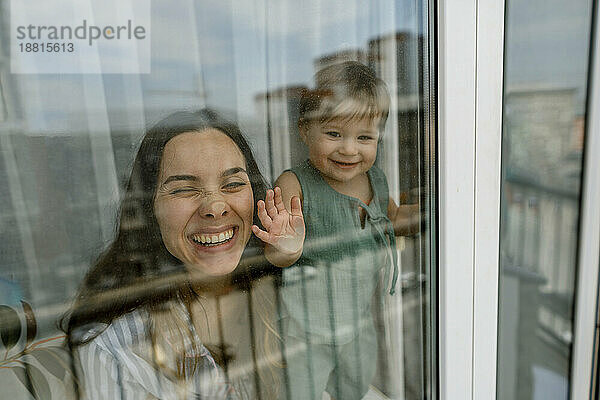 Glückliche Mutter und Tochter spielen am Fenster  durch Glas gesehen