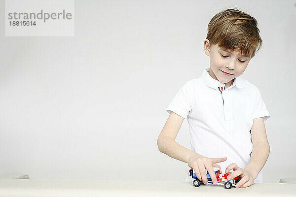 Blond boy playing with toy car in front of white wall
