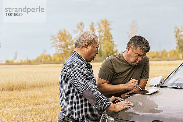 Mann benutzt Tablet-PC auf der Motorhaube seines Autos  zusammen mit seinem Vater auf einer Weizenfarm