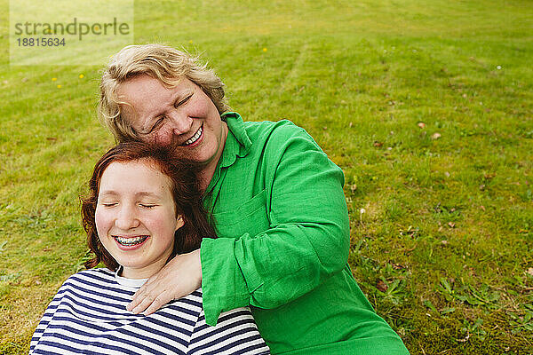 Glückliche Mutter umarmt Tochter  die auf Gras sitzt
