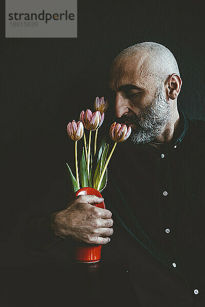 Reifer Mann riecht Blumen in Vase vor schwarzem Hintergrund