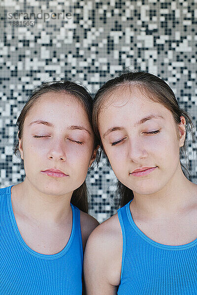 Twin sisters with eyes closed in front of textured wall