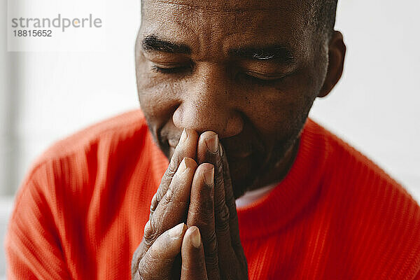 Reifer Mann betet mit gefalteten Händen und geschlossenen Augen