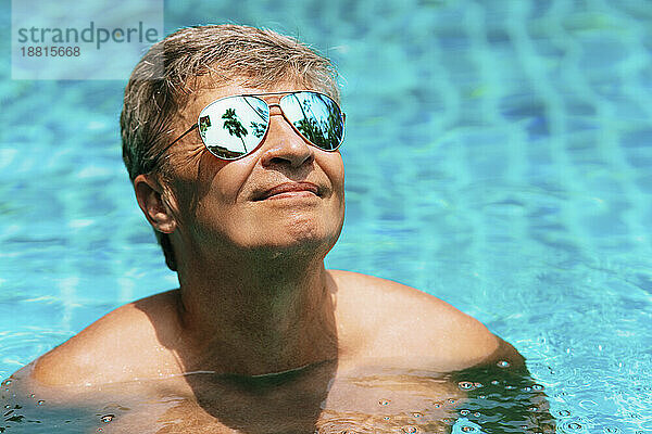 Lächelnder reifer Mann mit Sonnenbrille entspannt im Schwimmbad