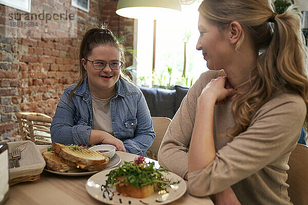 Glückliche Frau mit Down-Syndrom frühstückt mit Freundin im Café
