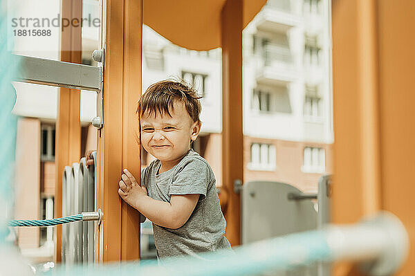 Lächelnder Junge steht auf Spielgeräten auf dem Spielplatz