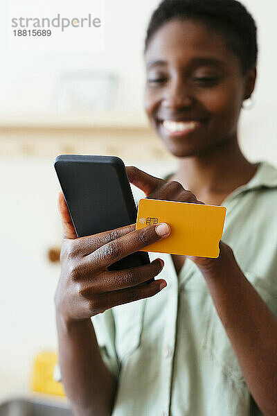 Lächelnde Frau  die zu Hause per Kreditkarte auf dem Mobiltelefon bezahlt
