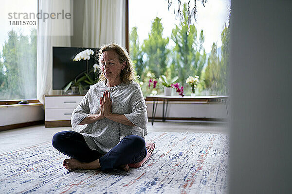 Ältere Frau mit gefalteten Händen praktiziert Meditation zu Hause