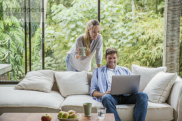 Glücklicher Freiberufler mit Laptop und Frau mit Kaffeetasse zu Hause