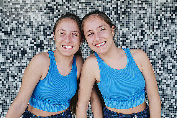 Glückliche Zwillingsschwestern vor strukturierter Wand