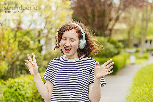 Fröhliches Mädchen mit kabellosen Kopfhörern  das singt und Musik hört