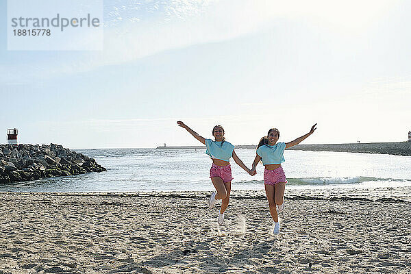 Sorglose Zwillingsschwestern halten Händchen und springen am Strand