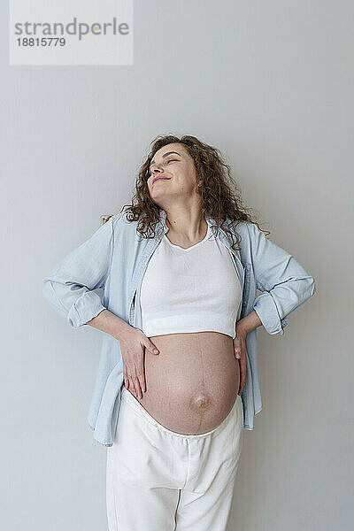 Smiling young pregnant woman standing in front of wall