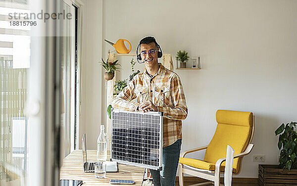 Lächelnder Geschäftsmann mit Solarpanel am Schreibtisch