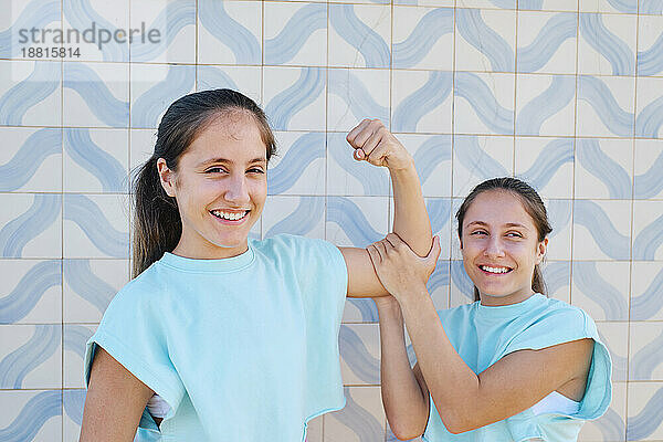 Glückliches Mädchen mit Schwester  die vor einer gemusterten Wand Muskeln spielen lässt