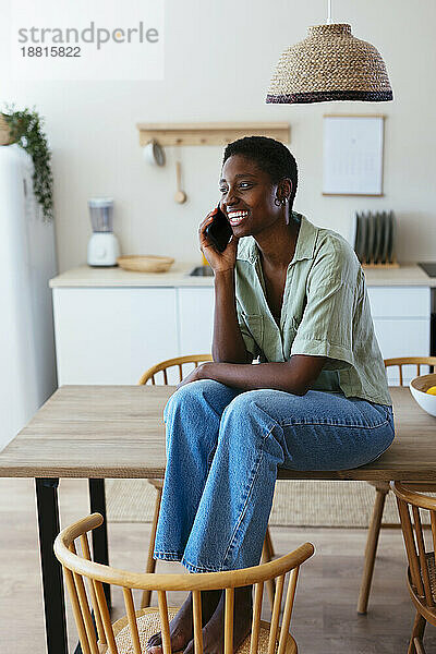 Glückliche Frau  die zu Hause in der Küche mit dem Smartphone spricht