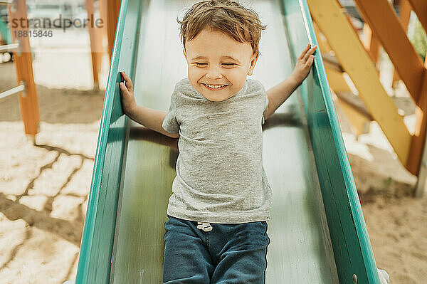Cheerful boy having fun on slide in playground