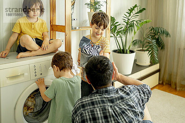 Vater und Kinder waschen zu Hause gemeinsam Wäsche in der Maschine