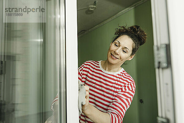 Lächelnde Frau putzt Fensterrahmen