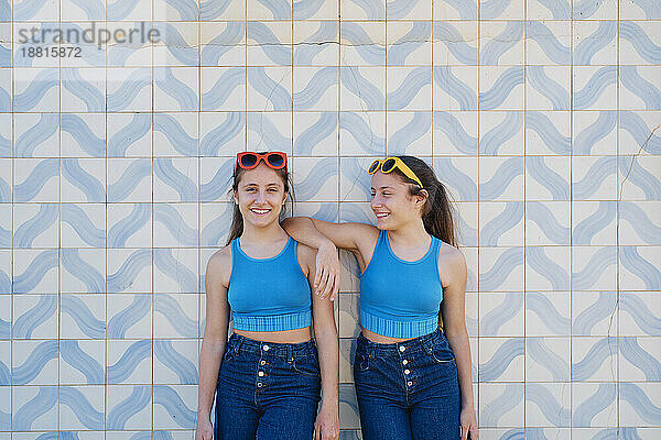 Glückliche Mädchen mit Sonnenbrille stehen vor der Wand