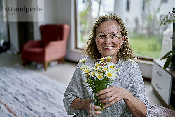 Glückliche ältere Frau mit Blumenvase zu Hause