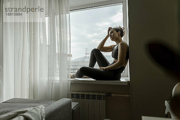 Nachdenkliche Frau entspannt sich zu Hause auf der Fensterbank