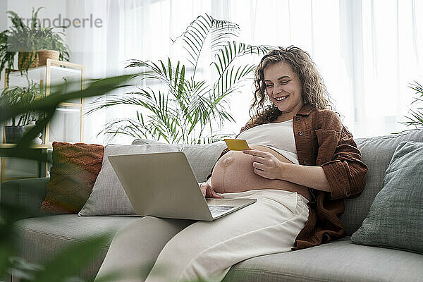 Lächelnde schwangere Frau  die zu Hause mit Kreditkarte online einkauft