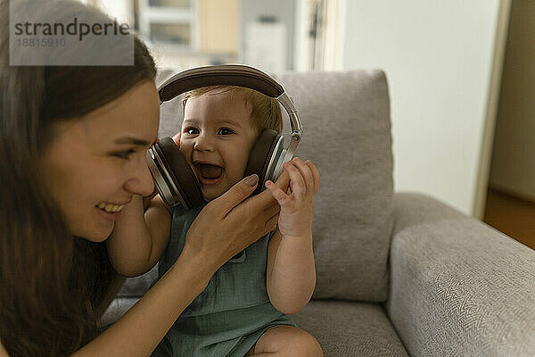 Glückliche Mutter gibt ihrem kleinen Mädchen zu Hause Kopfhörer