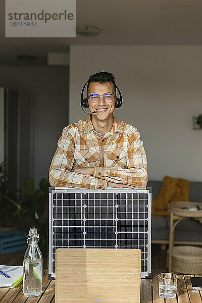 Lächelnder Geschäftsmann mit Solarpanel vor Laptop am Schreibtisch