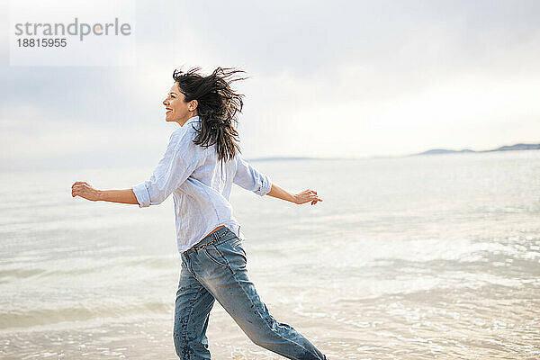 Reife  unbeschwerte Frau läuft am Strand am Meer