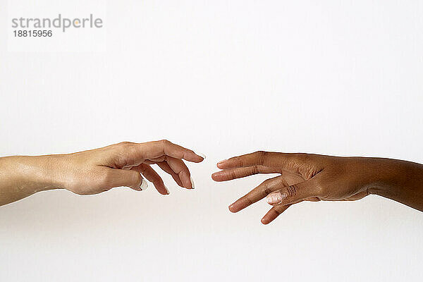 Cropped image of friends reaching to each other against white background