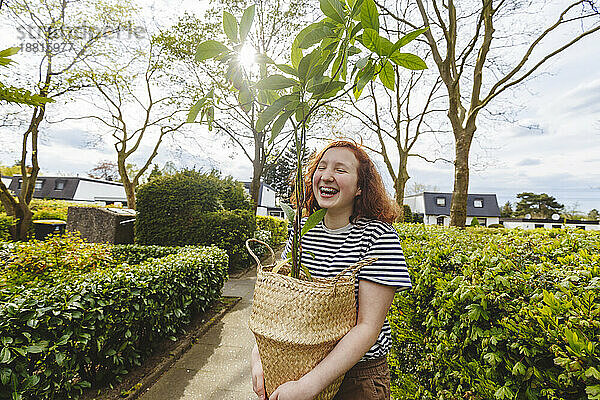 Fröhliches Mädchen steht mit Avocadopflanze auf Fußweg
