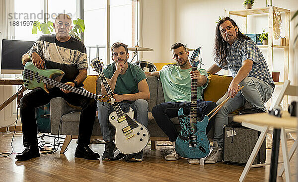 Rockmusiker sitzen mit Gitarren und Drumsticks zu Hause auf dem Sofa