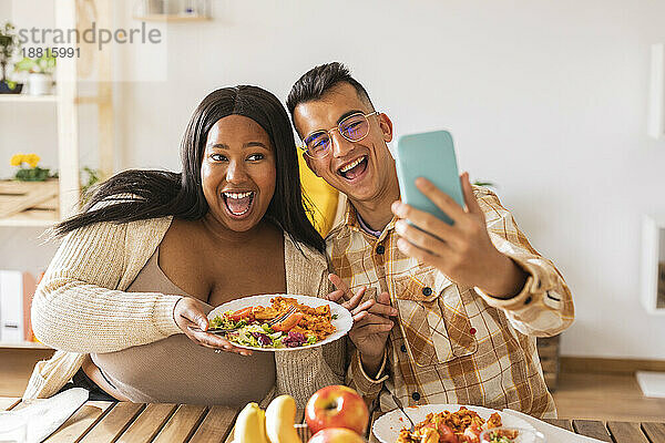 Glückliches Paar macht Selfie mit Essen am Esstisch