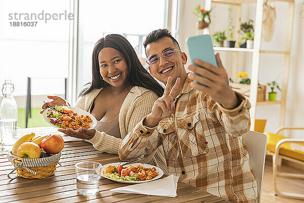 Glückliches Paar macht Selfie beim Essen am Esstisch