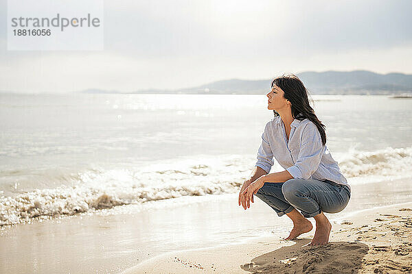 Mature woman crouching on sand at beach