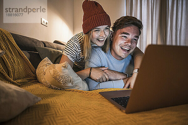 Liebevolles junges Paar benutzt Laptop im Wohnzimmer