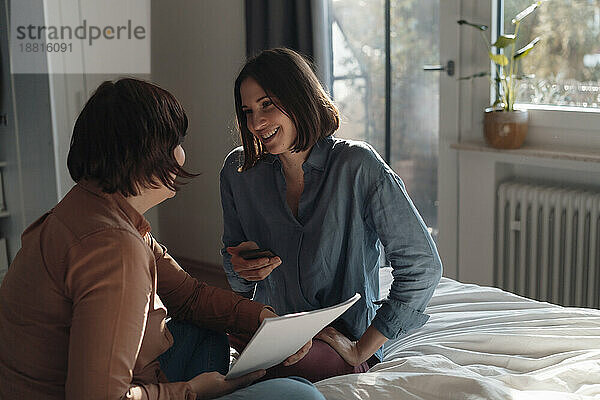 Lächelnde Frau spricht mit einer lesbischen Freundin  die zu Hause im Bett sitzt