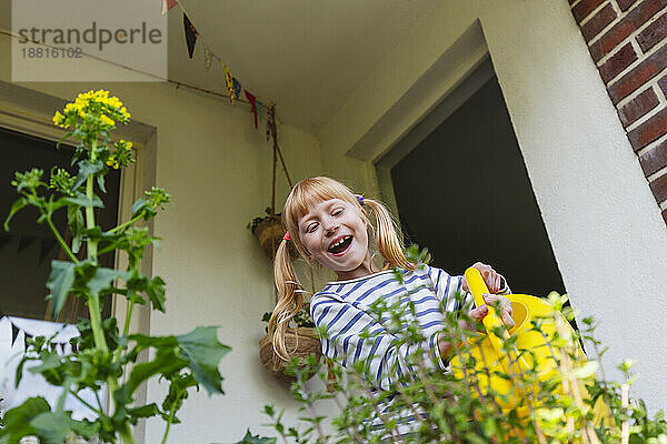 Glückliches Mädchen  das Pflanzen auf dem Balkon gießt
