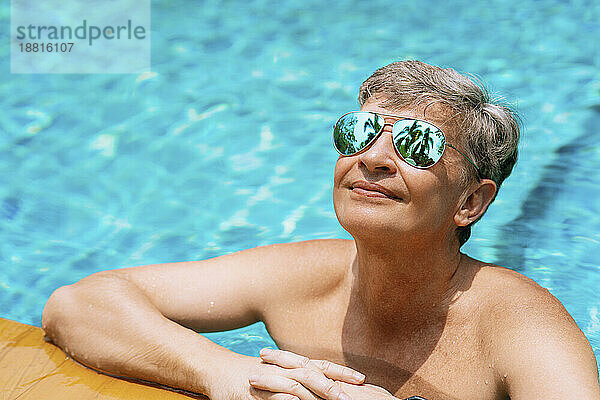Lächelnder Mann mit Sonnenbrille entspannt sich an einem sonnigen Tag im Schwimmbad