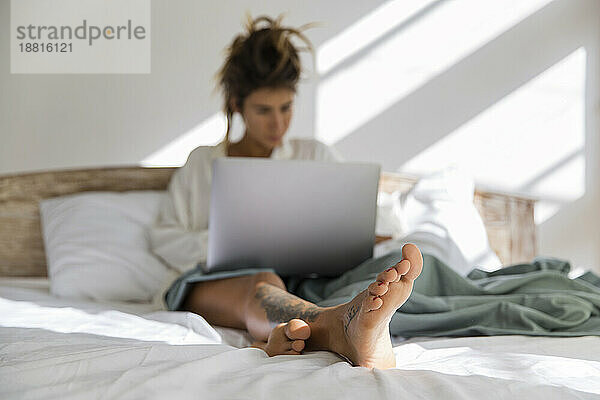 Frau sitzt mit Laptop zu Hause im Bett