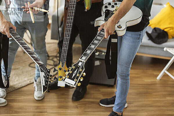 Musiker stehen mit Gitarren und Trommelstöcken zu Hause