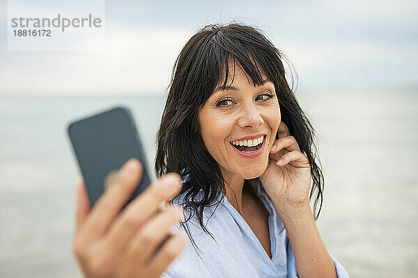 Fröhliche Frau  die am Strand ein Selfie mit ihrem Smartphone macht