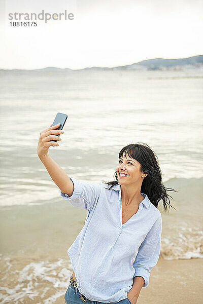 Lächelnde Frau  die am Strand ein Selfie mit dem Mobiltelefon macht