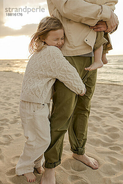 Lächelndes Mädchen umarmt Vater am Strand
